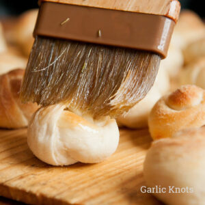 wooden brushing with bristles brushing butter on garlic roll