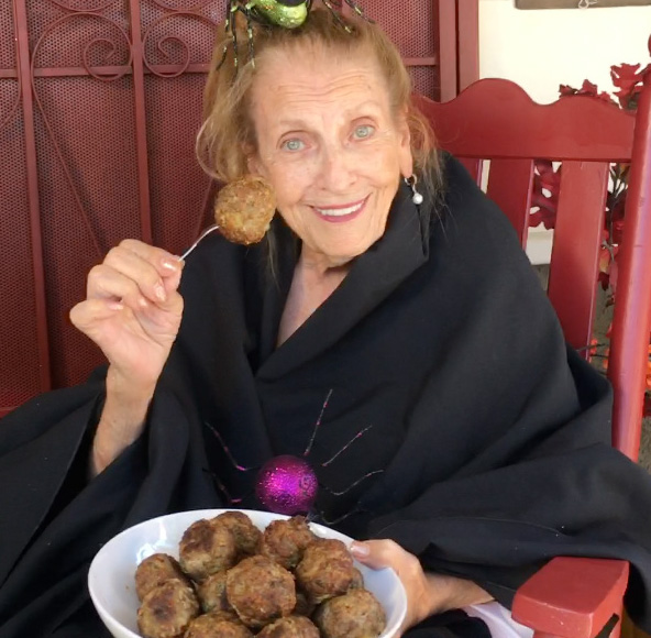 Maria smiling with a plate of meatballs, holding one up on a fork