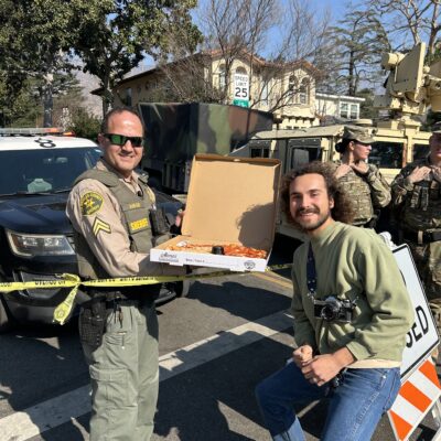 A first responder and photographer smiling sharing a pizza