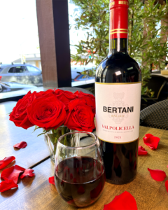 A bottle of Bertani next to a glass and a vase of red roses.