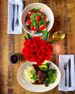 Bird's eye view of the caprese salad and short rib with a vase of red roses in the middle