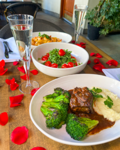 short rib, caprese salad, and shrimp pasta with a glass of white wine and rose petals