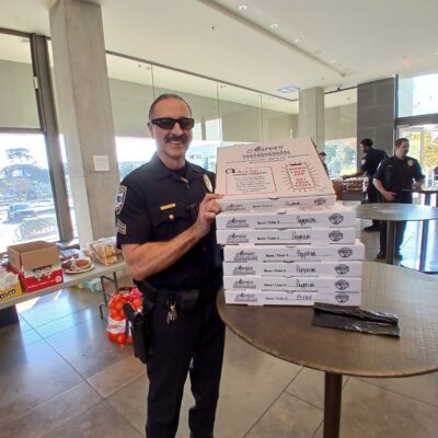 A first responder holding a few boxes of pizza, smiling