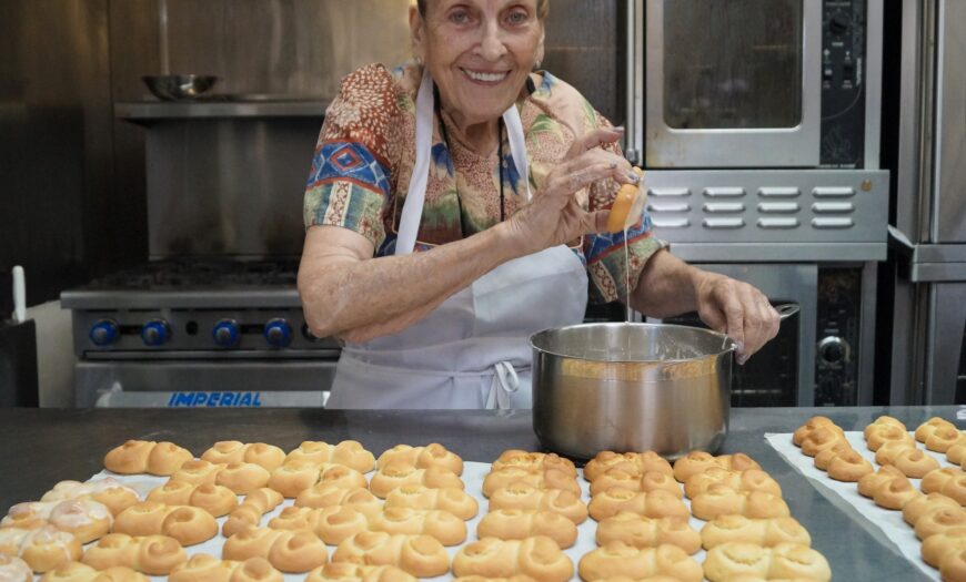 Maria, smiling, dipping fresh baked Italian cookies into white icing.