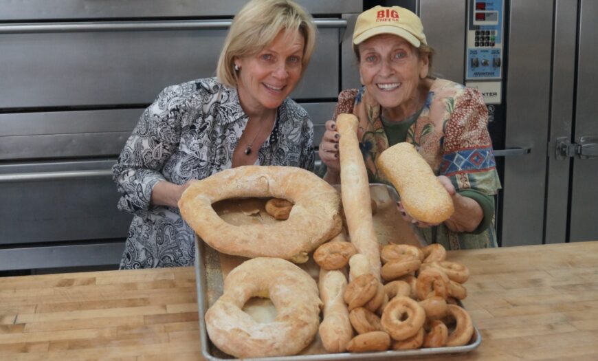 Maddy and her mother, Maria, smiling; displaying a tray of fresh baked bread.